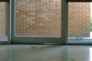 Image of metal framed exterior glass door with a large gap between the threshold and the door frame with daylight showing through the gap